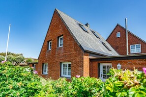 A two-story brick house with a steeply pitched roof, a chimney, and a small attached garage. - Strandberg II - 3-room apartment for up to 4 people - only 400 meters to the beach (Sylt)