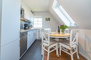 Une cuisine moderne avec des meubles blancs, une machine à café et un coin repas comprenant une table ronde et des chaises blanches.