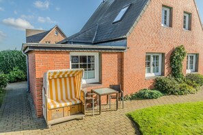 A brick house with a small patio area featuring a striped sofa and a table. - Strandberg II - 3-room apartment for up to 4 people - only 400 meters to the beach (Sylt)