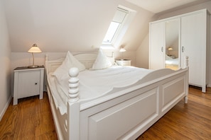 Une chambre à coucher avec un lit blanc, une table de chevet, une armoire et une lucarne.