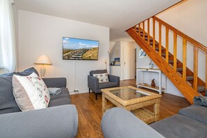 Ein modernes Wohnzimmer mit einem grauen Sofa, einem Korbtisch und einer Holztreppe.