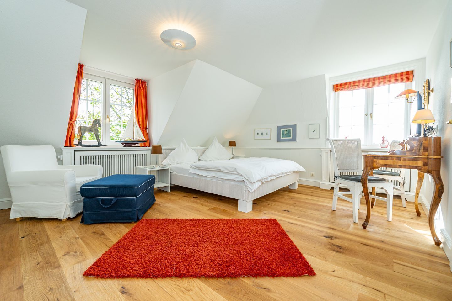 Ein Schlafzimmer mit Bett, Schreibtisch, Stuhl, Heizkörper und einem Fenster mit Vorhängen.