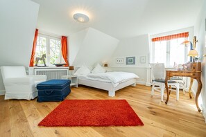 A bedroom with a bed, a desk, a chair, a radiator, and a window with curtains. - Wiip Hüs - Unter Reet Gebautes Hausteil in Keitum, mit Garten für bis zu 4 Personen (Sylt-Ost)