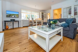 Un salon moderne avec une table basse en verre, un canapé gris et un téléviseur diffusant un paysage pittoresque.