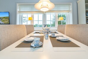A dining area with a white table set for four, two lamps, and a view of greenery outside. - Wiip Hüs - Unter Reet Gebautes Hausteil in Keitum, mit Garten für bis zu 4 Personen (Sylt-Ost)