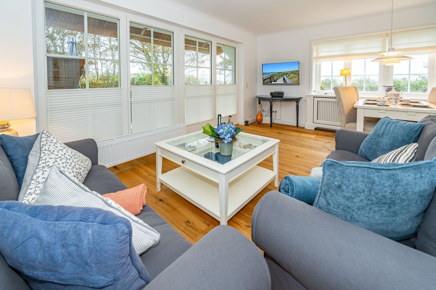 Ein modernes Wohnzimmer mit einem Glastisch, grauen Sofas und einem Fernseher auf einem Standfuß.