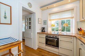 A modern kitchen with a built-in oven, a window with a view of greenery, and a wooden countertop. - Wiip Hüs - Unter Reet Gebautes Hausteil in Keitum, mit Garten für bis zu 4 Personen (Sylt-Ost)