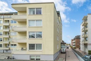 Un immeuble résidentiel à plusieurs étages, doté de balcons, d’un espace de stationnement et surplombant un ciel dégagé.