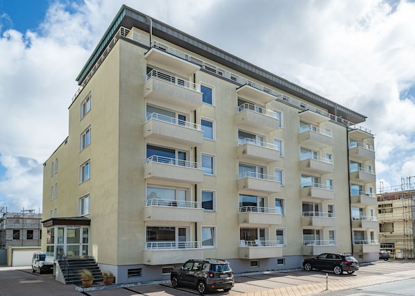Un immeuble à plusieurs étages doté de balcons, avec une entrée au niveau du sol et des voitures garées.