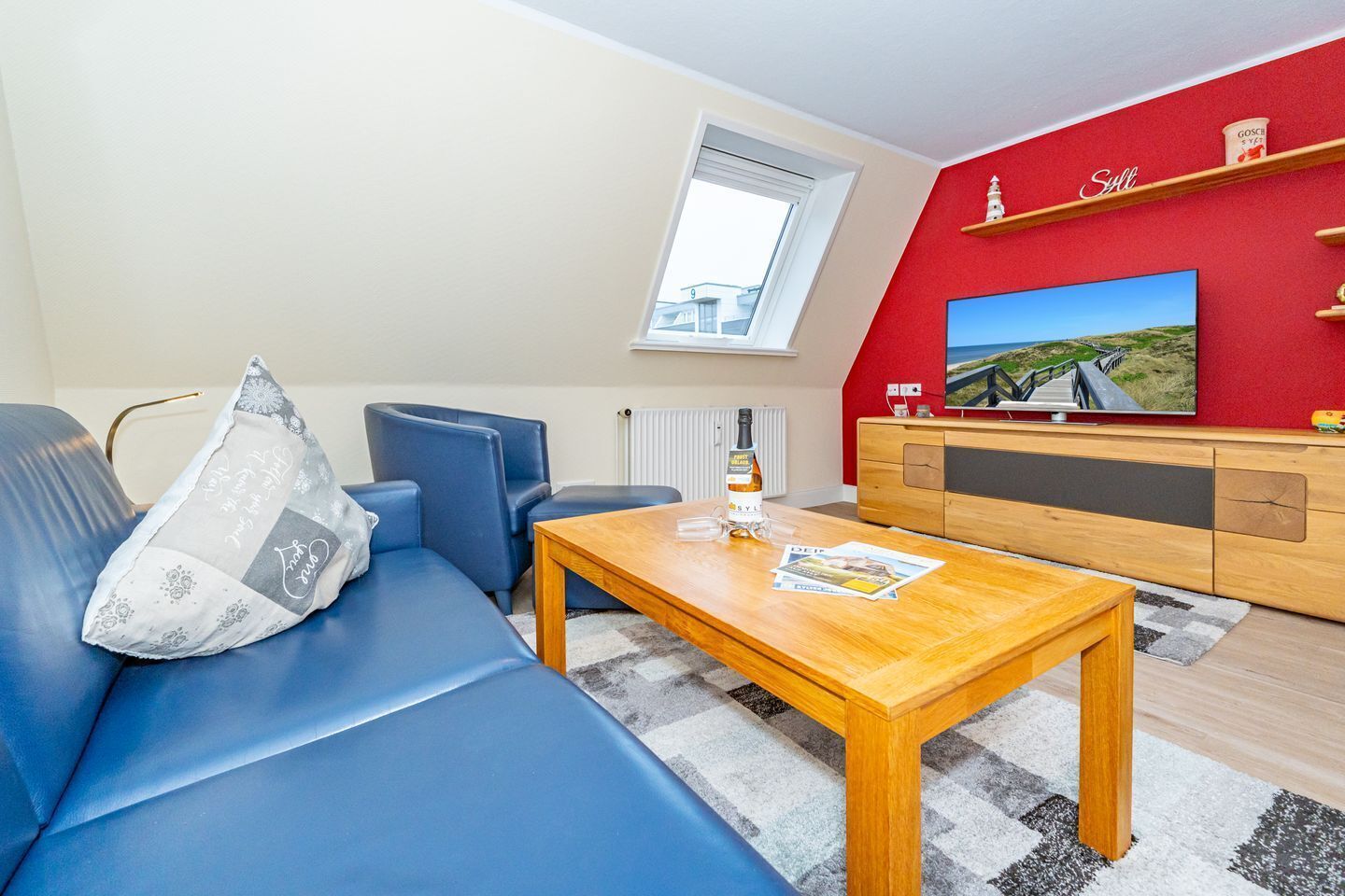 Uma sala de estar moderna com um sofá azul, uma mesa de centro de madeira, uma televisão em uma parede vermelha e uma janela.