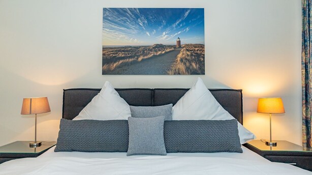 Hotelkamer met een groot bed, twee nachtkastjes, een hoofdbord en een aan de muur hangend schilderij van een vuurtoren.