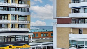 A multi-story building with balconies, a visible ground floor with signage, and a view of the sea in the background. - Strandmuschel App. 309 - Kleine, Geschmackvoll Eingerichtete Wohnung in Westerland, Direkt am (Sylt)