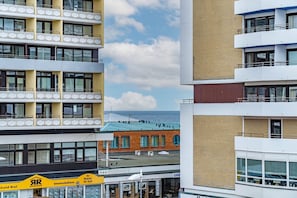 A multi-story building with balconies, a visible ground floor with signage, and a view of the sea in the background.