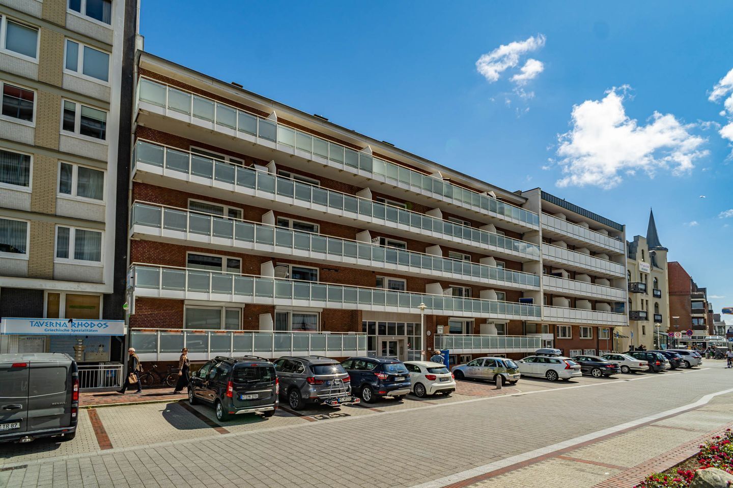 Ein mehrstöckiges Hotel mit Balkonen, einem Parkplatz und blauem Himmel.