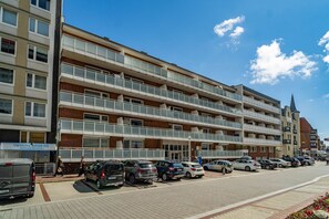 Un hotel de varios pisos con balcones, un estacionamiento y un cielo azul despejado.