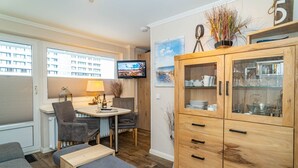 A modern kitchen with a dining area, a wooden cabinet with glass doors, and a television mounted on the wall. - Strandmuschel App. 309 - Kleine, Geschmackvoll Eingerichtete Wohnung in Westerland, Direkt am (Sylt)