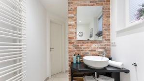 A modern bathroom with a white sink, a mirror, and a brick wall. - Wandaful Hüs - Holiday home for max. 4 persons, in a quiet location with (Sylt)