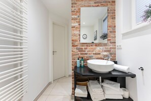 A modern bathroom with a white sink, a mirror, and a brick wall.