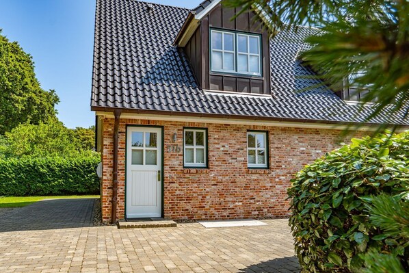 A two-story brick house with a dark tiled roof, a white door, and two windows.