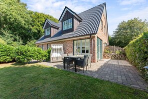 A two-story house with a brick exterior, a tiled roof, and a paved patio with outdoor furniture.