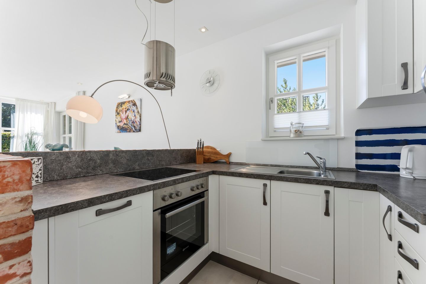 A modern kitchen with white cabinets, a black stove, and a window with a view of greenery.