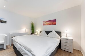 A modern bedroom with a large bed, bedside tables, a desk, and a chair.