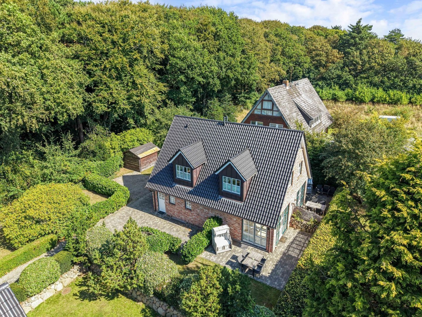 A house with a sloped roof, a brick exterior, and a paved patio with outdoor furniture.