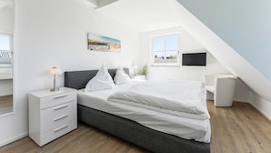 A modern bedroom with a bed, bedside table, lamp, and a painting on the wall. - Wandaful Hüs - Holiday home for max. 4 persons, in a quiet location with (Sylt)