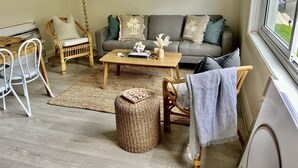 A cozy living room with a grey sofa, wicker chairs, a wooden coffee table, and a view of the outdoors through a window. - Little Manly 3 bedroom Oasis (Manly)