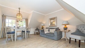 A cozy loft-style living room with a dining area, a grey sofa, and a chandelier. - Roseneck App. 6 - Cozy vacation apartment for up to 2 persons with (Sylt-Ost)