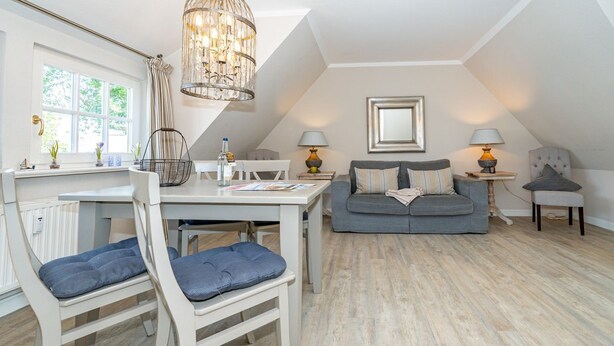 A spacious loft with a dining area, a gray sofa, and a chandelier. - Roseneck App. 6 - Cozy vacation apartment for up to 2 persons with (Sylt-Ost)