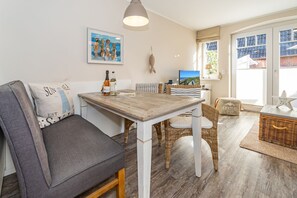 Ein gemütlicher Wohnbereich mit grauem Sofa, einem Holztisch, Korbstühlen und Blick auf das Meer durch große Fenster.