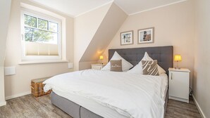 A bedroom with a large bed, two bedside tables with lamps, a window with blinds, and a sloped ceiling.