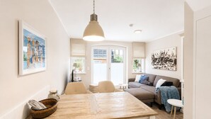 A modern living room with a wooden dining table, a sofa, and a hanging light fixture.