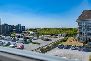 Ein Parkplatz mit mehreren Autos und Wohnmobilen, ein Gebäude mit Balkonen und ein Hügelgrün.