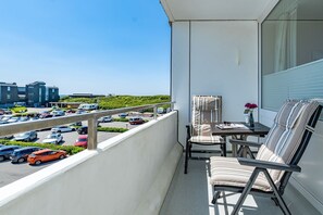Un balcon avec une table et des chaises, donnant sur un parking et des immeubles.