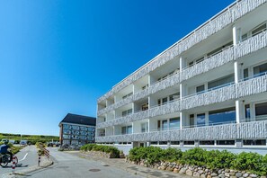 Un hôtel à plusieurs étages doté de balcons, d’une allée pavée et surplombant un ciel d’un bleu limpide.