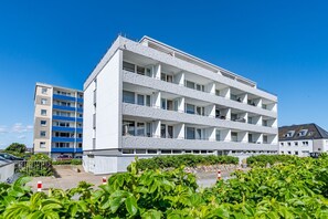 A multi-story residential building with balconies, a parking area, and surrounding greenery. - App. Sonnenzauber - 1-room vacation apartment with balcony in Westerland, directly on the (Sylt)