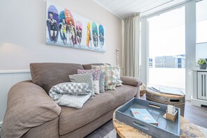 A living room with a sofa, pillows, a tray table, and a painting of surfers. - App. Sonnenzauber - One-room vacation apartment with a balcony in Westerland, right on the (Sylt)
