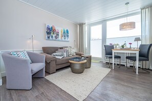 A modern living room with a sofa, a coffee table, and a dining area with a table and chairs. - App. Sonnenzauber - 1-room vacation apartment with balcony in Westerland, directly on the (Sylt)