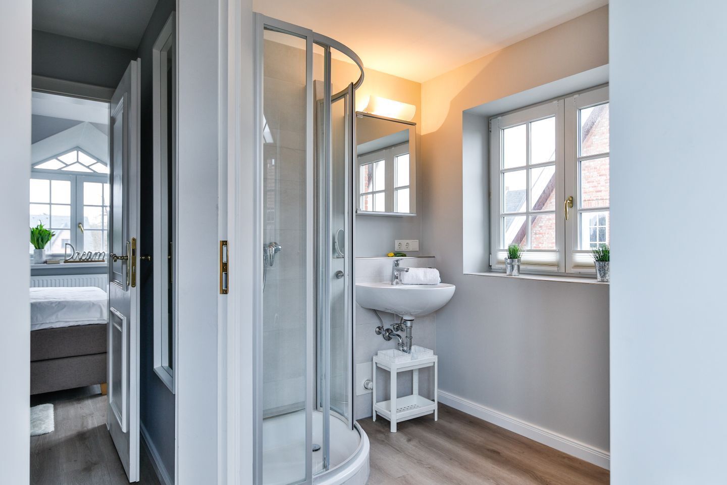 A modern bathroom with a glass shower enclosure, a white sink, and a window with a view of the outside.