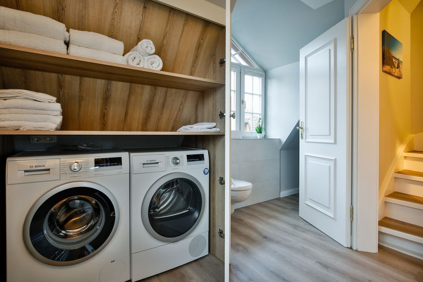 A laundry area with two Bosch washing machines and a shelf with neatly folded towels.
