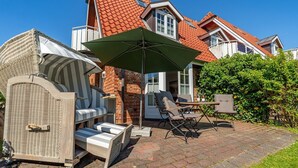 Eine Terrasse mit Gartenmöbeln, einem großen Sonnenschirm und einem Backsteinhaus im Hintergrund.