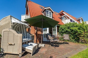 Un espace patio aménagé avec du mobilier d’extérieur, un grand parasol et une maison en briques en arrière-plan.