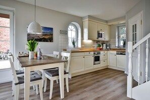 Una cocina con armarios blancos, encimera de madera y comedor con sillas blancas y una mesa de madera.