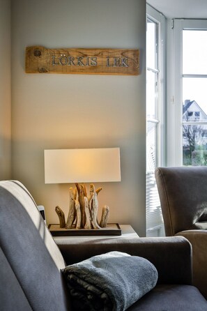 A cozy living room with a wooden sign above a lamp, a window with blinds, and a grey sofa.