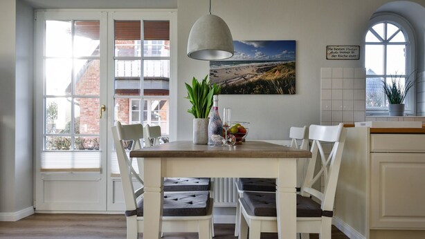 Ein Essbereich mit Holztisch, weißen Stühlen, einer Pendelleuchte, einem Blumentopf und einem gerahmten Bild an der Wand.