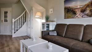 Ein Wohnzimmer mit braunem Ledersofa, einem weißen Couchtisch, einer Lampe und einem Gemälde mit einer Strandansicht.