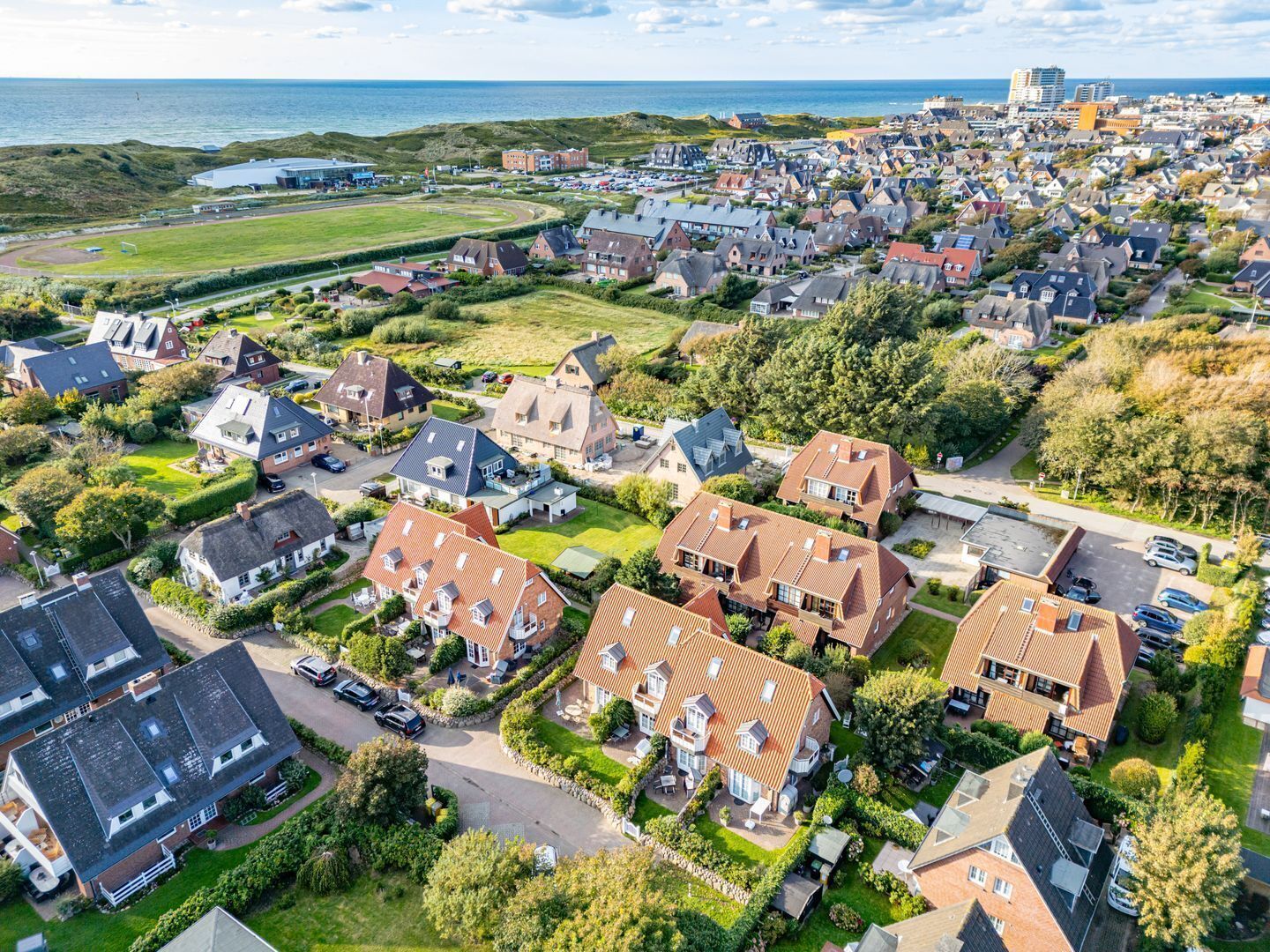 An aerial view of a residential area with houses, a large building in the distance, and a coastline.