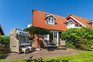 Una casa con techo de tejas rojas, fachada de ladrillo y un patio con mobiliario exterior y una zona de estar cubierta.